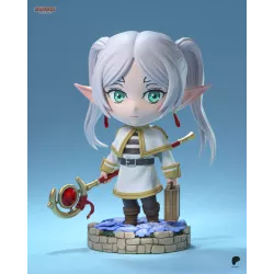 Frieren en version chibi, avec son bâton magique et sa mallette, sur un socle fleuri au rendu délicat.