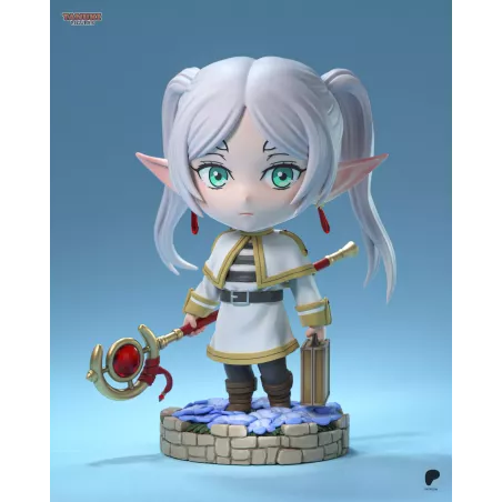 Frieren en version chibi, avec son bâton magique et sa mallette, sur un socle fleuri au rendu délicat.