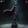 Re-L Mayer représentée debout sur son socle, vêtue de son corset violet, de son pantalon ajusté et de son long manteau flottant.