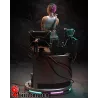 La figurine présentée dans son environnement technologique, entourée d’écrans, de câbles et d’éclairages néon futuristes.