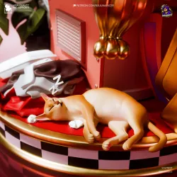 À l’arrière du socle, un petit chat sommeille paisiblement parmi les vêtements et les bagages